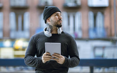 Hipster-Mann mit Kopfhörern hält digitales Tablet und schaut weg - JCCMF01251