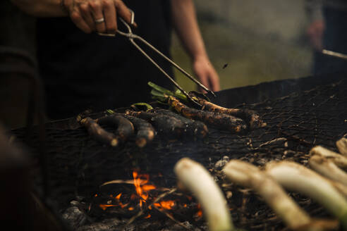 Jugendlicher mit Servierzange beim Kochen von Scallions auf dem Grill im Freien stehend - ACPF01155