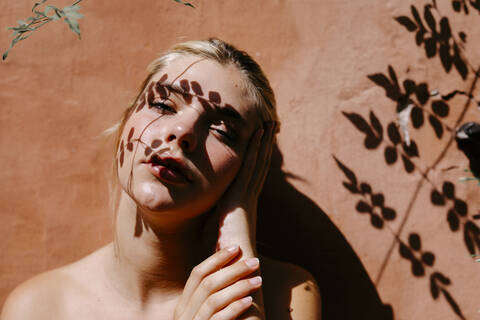 Sinnliche Frau gegen Wand mit Blätter Schatten auf Gesicht, lizenzfreies Stockfoto