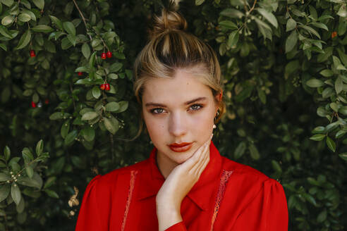 Beautiful blond woman with hand on chin against plants - TCEF01539