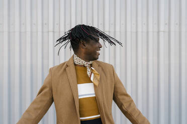 Lächelnder afrikanischer Mann, der sein Haar gegen eine graue Wand wirft - EGAF01796