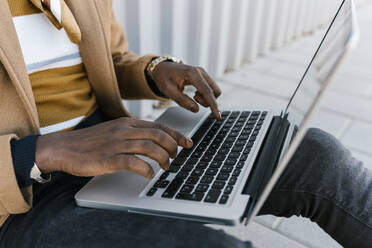 Man using laptop while sitting against gray wall - EGAF01798