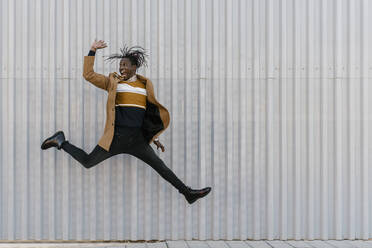 Cheerful man jumping against gray wall - EGAF01803