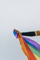 Afrikanischer Mann hält LGTBQI-Flagge gegen weiße Wand - EGAF01820