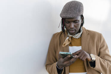 Afrikanischer Mann benutzt ein Smartphone an einer weißen Wand - EGAF01823