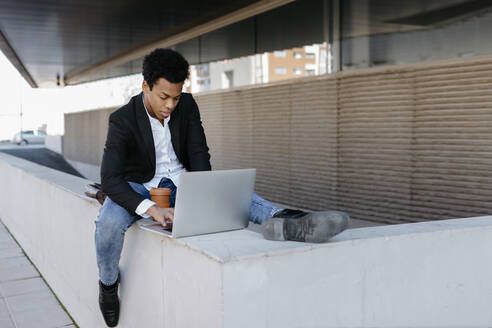 Mittlerer erwachsener Geschäftsmann, der einen Laptop benutzt, während er auf einer Stützmauer sitzt - TCEF01542