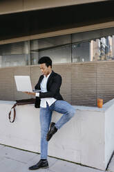 Mittlerer erwachsener Geschäftsmann, der auf einem Bein steht und einen Laptop benutzt - TCEF01545