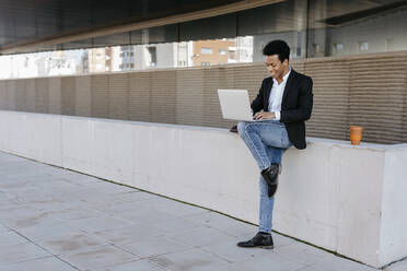 Male entrepreneur using laptop while standing on one leg against retaining wall - TCEF01546