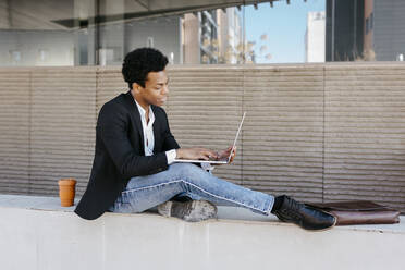 Male businessman using laptop while sitting on retaining wall - TCEF01553