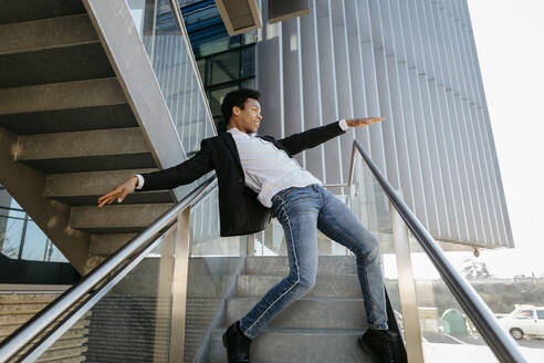 Männlicher Tänzer mit ausgestreckten Armen tanzt, während er sich auf ein Treppengeländer stützt - TCEF01571