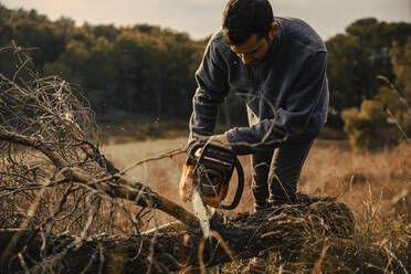Teenage boy cutting wood with chainsaw in forest - ACPF01157