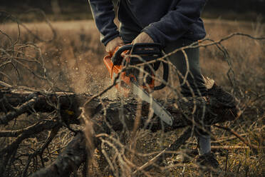 Teenage boy cutting tree trunk with chainsaw in forest - ACPF01158