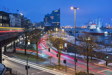 Germany, Hamburg, Vehicle light trails stretching along harbor street at dawn with Elbphilmarmonie in background - RJF00867