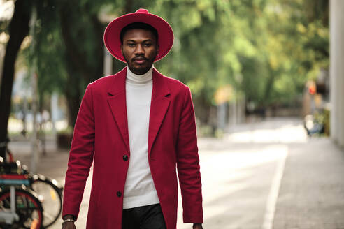 Confident fashionable man walking outdoors during sunny day - AGOF00065