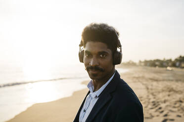 Afro-Mann mit Kopfhörern am Strand an einem sonnigen Tag - JRFF05046