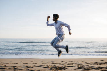 Mittlerer erwachsener Mann springt am Strand während eines sonnigen Tages - JRFF05052