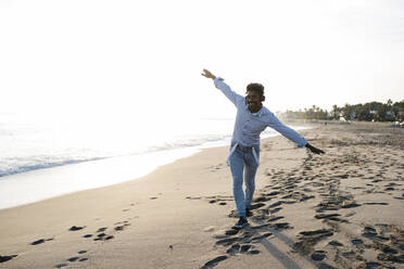 Playful man imitating airplane while while walking at beach - JRFF05055