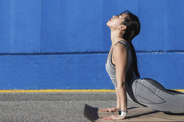 Frau macht Urdhva Mukha Svanasana an der blauen Wand - PNAF00661