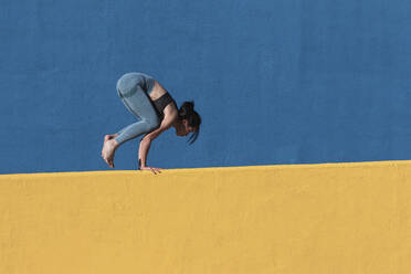 Strong woman doing handstand by wall - PNAF00676