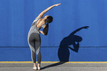Frau in Sportkleidung bei einer Übung vor einer blauen Wand - PNAF00684