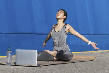Frau mit ausgestreckten Armen macht Yoga vor einem Laptop - PNAF00691