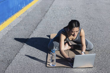 Woman using laptop while sitting on footpath - PNAF00692