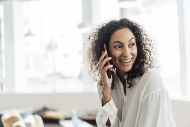 Smiling businesswoman talking on mobile phone while sitting at cafe - JOSEF03446