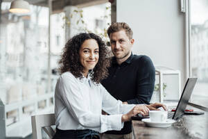 Confident businesswoman sitting by colleague with laptop at cafe - JOSEF03450