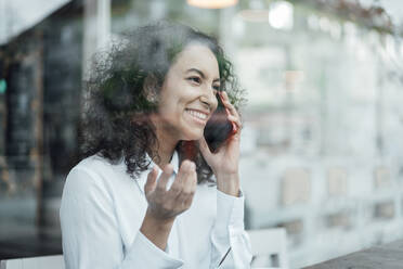 Junge Geschäftsfrau lächelt, während sie in einem Café sitzt und mit ihrem Handy spricht - JOSEF03461