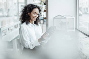 Junge Geschäftsfrau lächelt, während sie in einem Café sitzt und ein digitales Tablet benutzt - JOSEF03463
