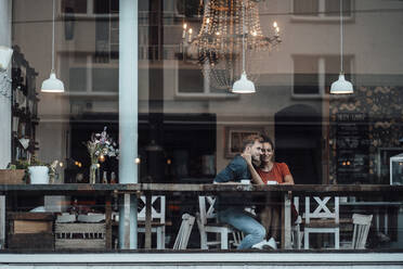 Junge Frau mit Arm um einen Mann, der am Fenster eines Cafés sitzt - JOSEF03466