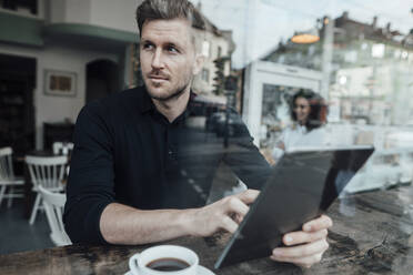 Geschäftsmann, der ein digitales Tablet benutzt und wegschaut, während er in einem Café sitzt - JOSEF03471
