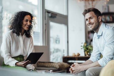 Geschäftsfrau mit digitalem Tablet, die einen Kollegen ansieht, während sie in einem Cafe sitzt - JOSEF03472