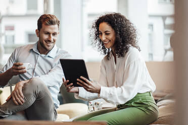 Smiling businesswoman using digital tablet while sitting with colleague at cafe - JOSEF03474