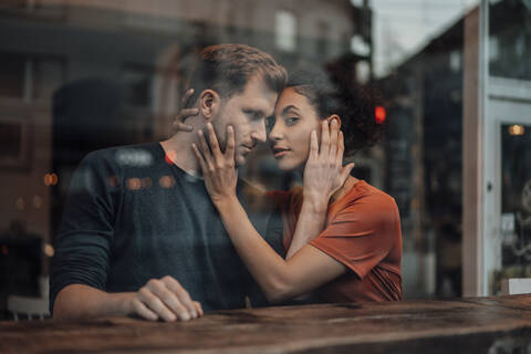 Romantic couple touching each others faces at cafe seen through window stock photo