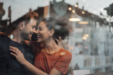 Smiling couple rubbing noses while sitting by cafe window - JOSEF03482