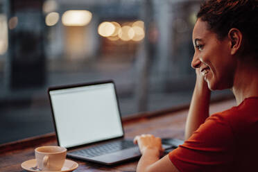 Lächelnde Frau, die einen Laptop benutzt, während sie in einem Café sitzt - JOSEF03486