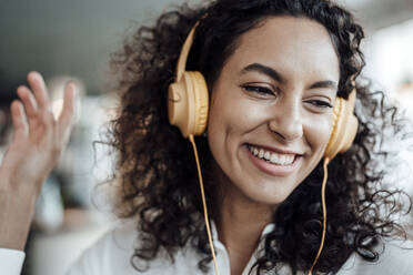 Happy businesswoman wearing headphones smiling while listening music at cafe - JOSEF03491