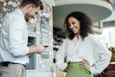 Businessman using mobile phone while standing by colleague at cafe - JOSEF03499