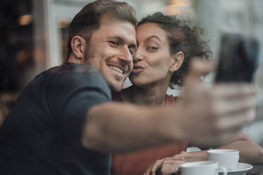 Lächelnder Freund nimmt Selfie mit Freundin durch Handy beim Sitzen im Café - JOSEF03511