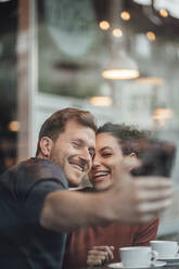 Happy couple taking selfie through mobile phone while sitting at cafe - JOSEF03512
