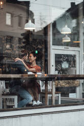 Lächelnde Frau, die einen Mann ansieht, während sie in einem Café sitzt und den Arm um ihn legt - JOSEF03514