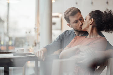 Junge Frau küsst Mann beim Zusammensitzen in einem Cafe - JOSEF03519