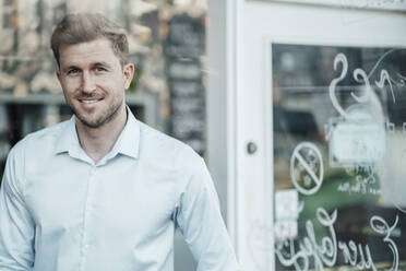 Männlicher Unternehmer lächelt, während er im Cafe steht - JOSEF03541