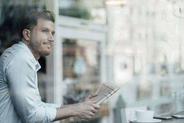 Businessman with newspaper looking away while standing at cafe - JOSEF03545