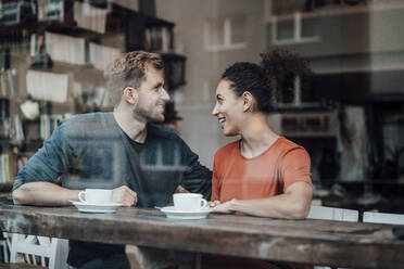 Lächelndes Paar, das sich gegenseitig ansieht, während es am Fenster eines Cafés sitzt - JOSEF03560