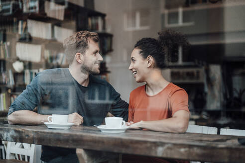 Lächelndes Paar, das sich gegenseitig ansieht, während es am Fenster eines Cafés sitzt - JOSEF03560