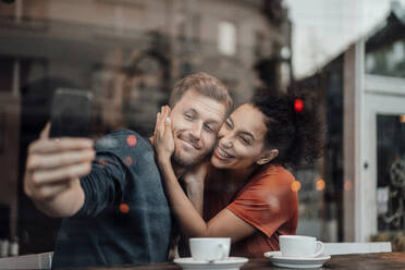 Freund nimmt Selfie mit Freundin durch Handy beim Sitzen im Cafe - JOSEF03563