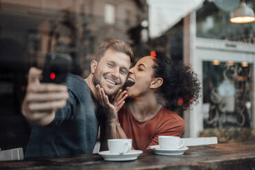 Lächelnder Freund nimmt Selfie durch Handy mit Freundin beim Sitzen im Cafe - JOSEF03564