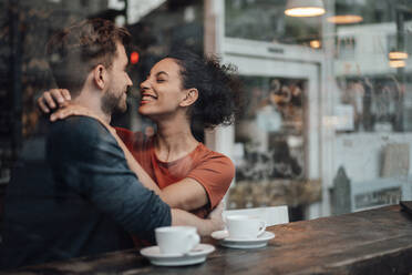 Romantic couple smiling while sitting with arm around on each other at cafe - JOSEF03569